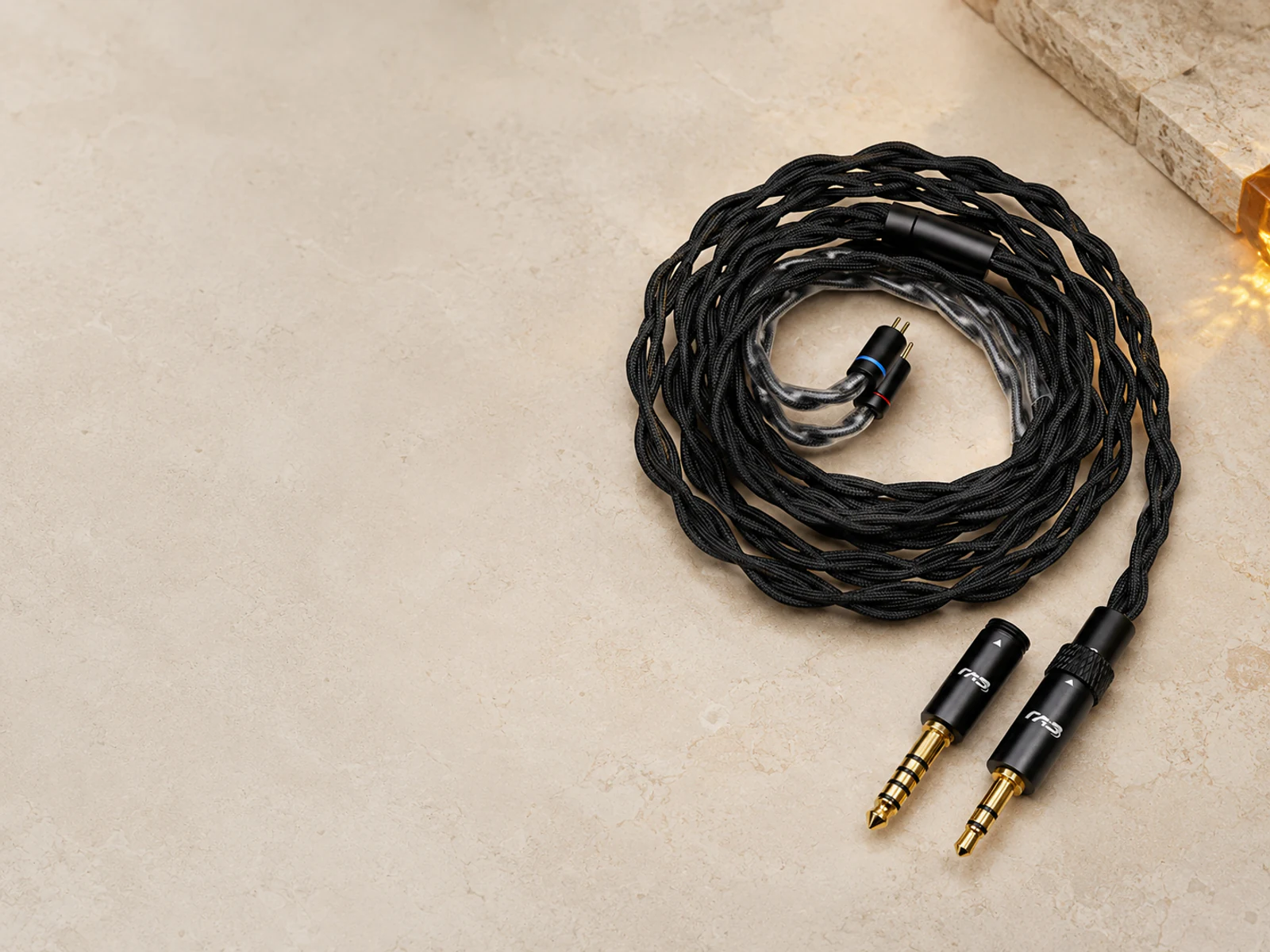 Cable de audio negro trenzado con conectores dorados sobre una superficie de piedra clara