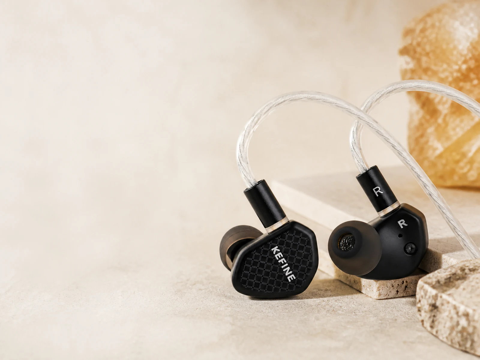 IEMs KEFINE negros con cable transparente en un estudio de tonos marfil